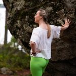 Nainen seisoo metsässä nojaten suureen kiveen ja katsoo järvelle – kehoteot voivat olla pieniä, arkeen mahtuvia hetkiä kehon äärellä.